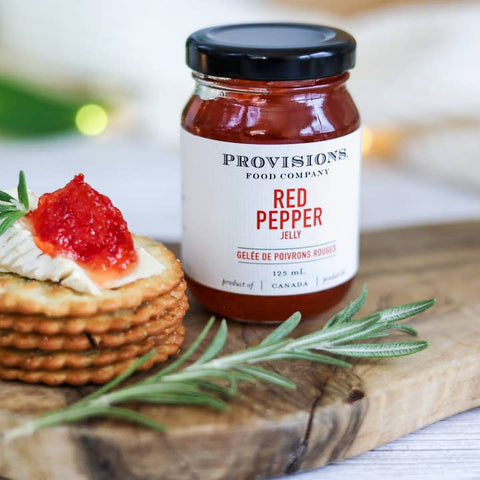 Jar of Provisions Red Pepper Jelly on a wooden board with crackers and herbs