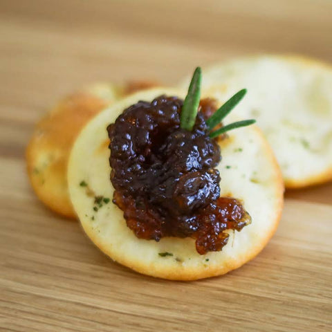 Cracker with dark spread and rosemary on a wooden surface