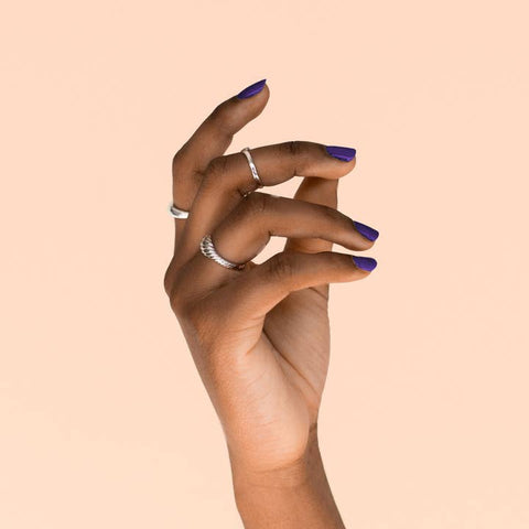 Hand with purple nail polish on a beige background