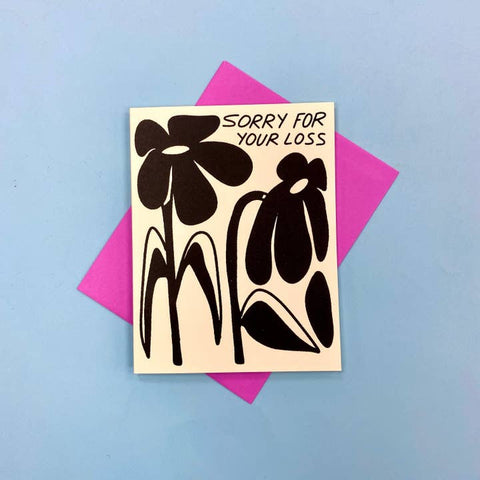 Card with black floral design and 'Sorry for your loss' text on a pink card against a blue background