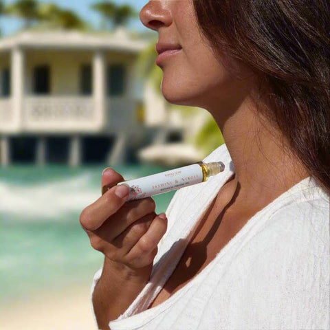 Woman holding a cosmetic product with a blurred beach and house in the background