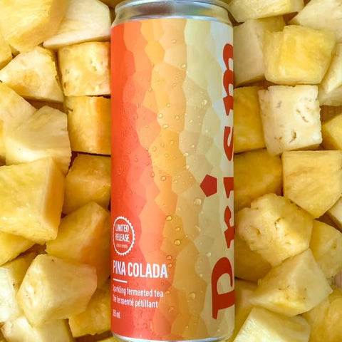 A can of Prizm Pika Colada flavored fermented tea surrounded by fresh pineapple chunks.