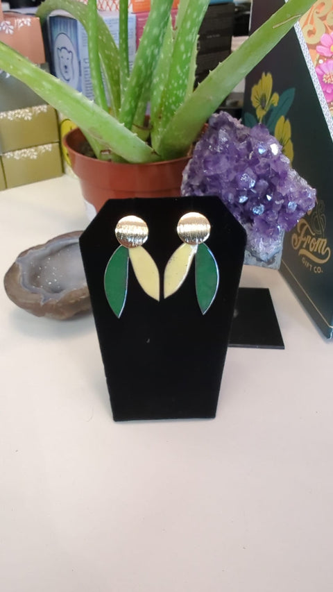 Pair of earrings on a black earring stand with a plant and decorative items in the background.