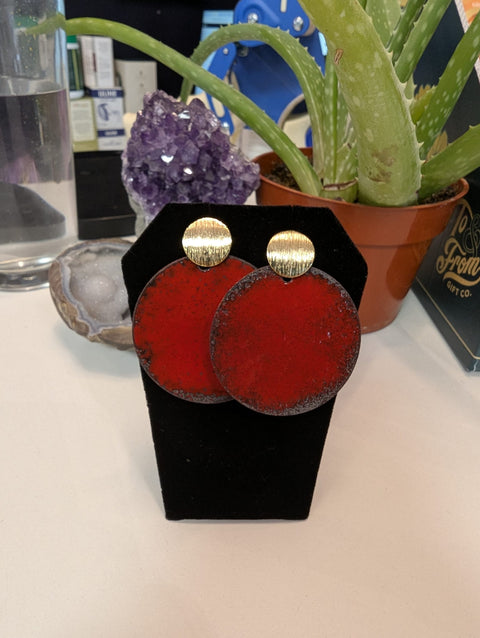 Red earrings with gold tops on a black stand, surrounded by decorative items.