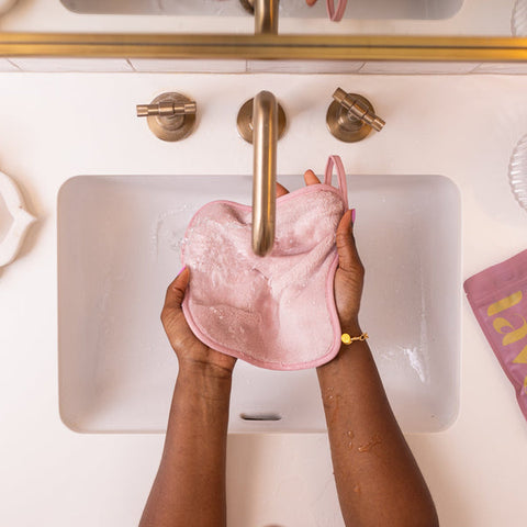Person holding a pink reusable pad over a sink with a mirror above.