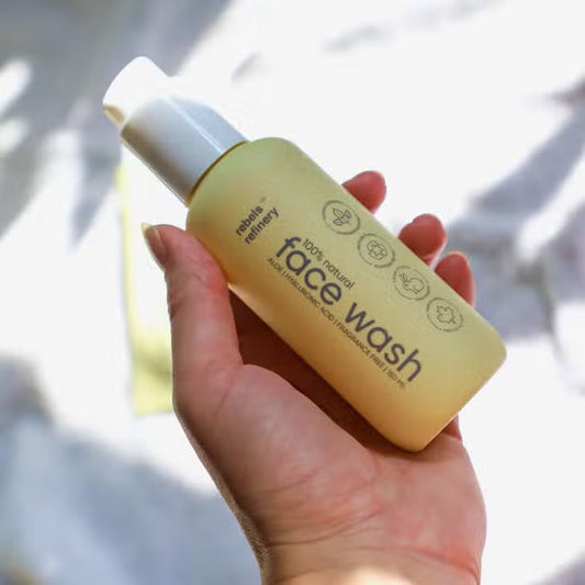 hand holding yellow bottle of rebel refinery 100% natural face wash in pump bottle.