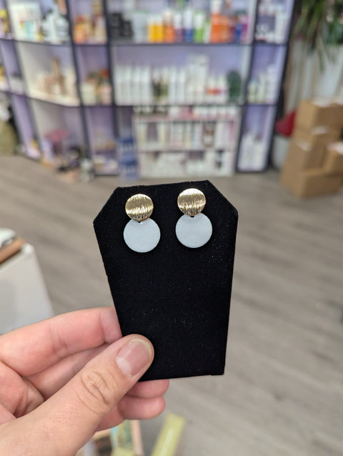 Pair of earrings on a black stand held by a hand with a blurred store background
